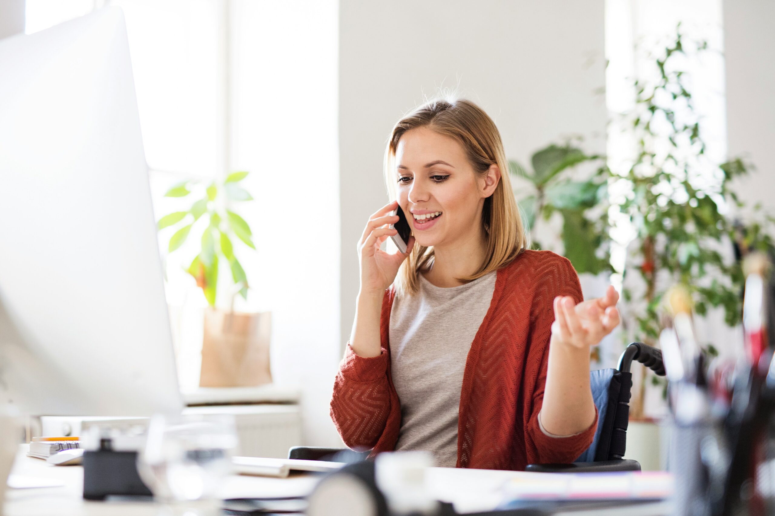 A professional woman smiling while talking on a phone at a modern office desk, representing the clear communication provided by a US-based answering service.